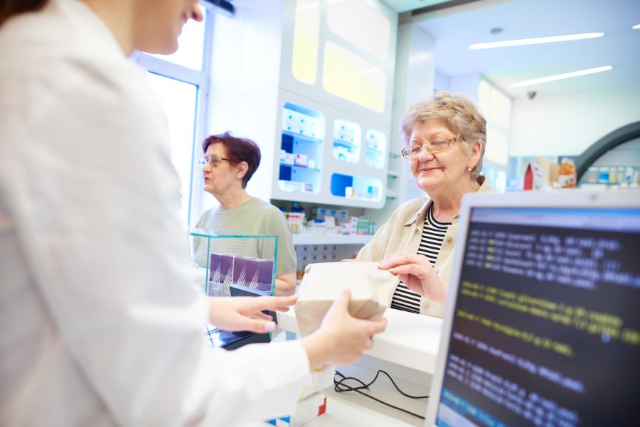 A woman purchases medications at a pharmacy counter, unaware that the data entered into the computer screen next to her could be compromised in violation of HIPAA regulations.
