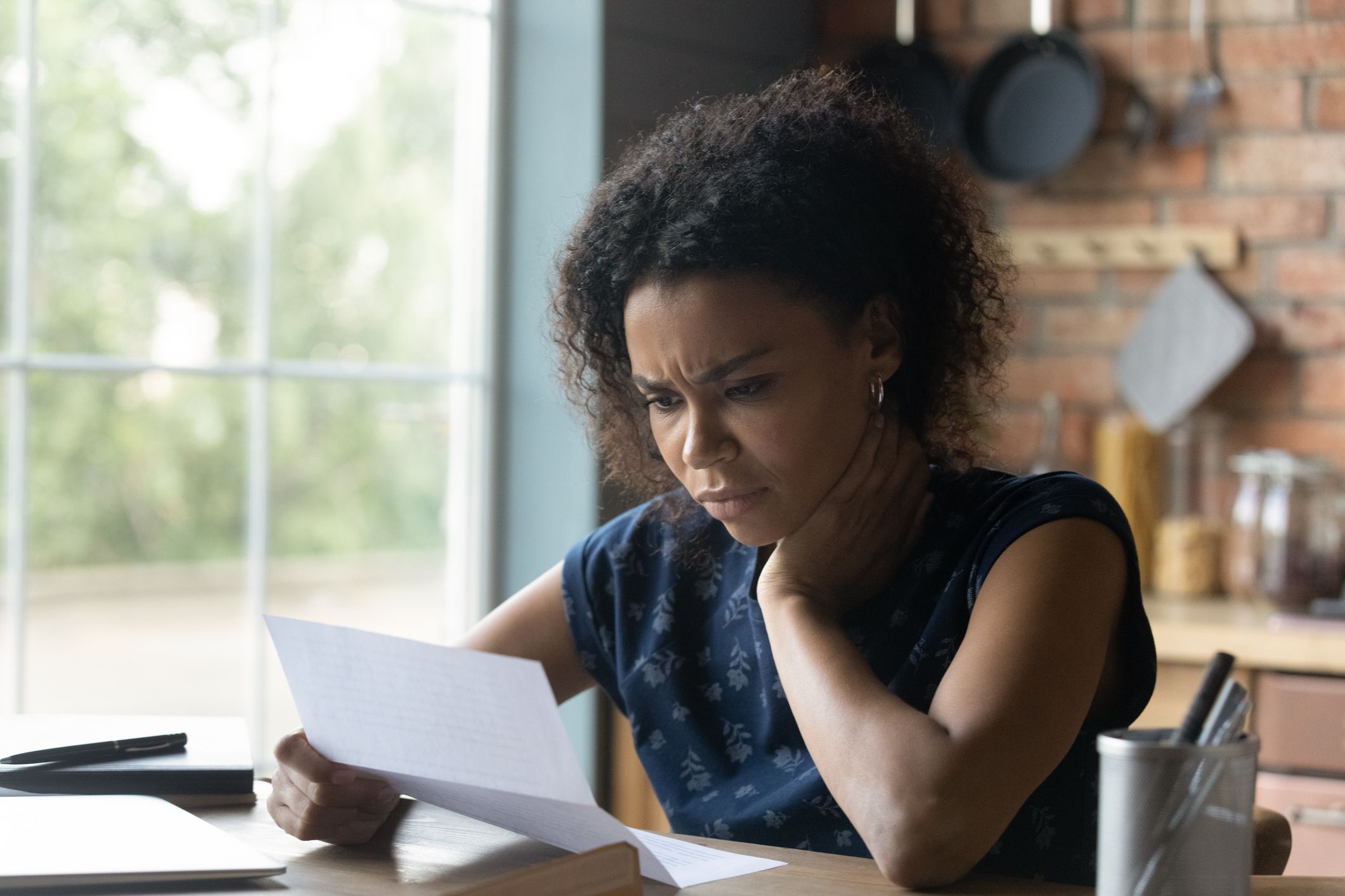 A woman with curly hair sits at her kitchen table and frowns at unexpected charges on her bill.