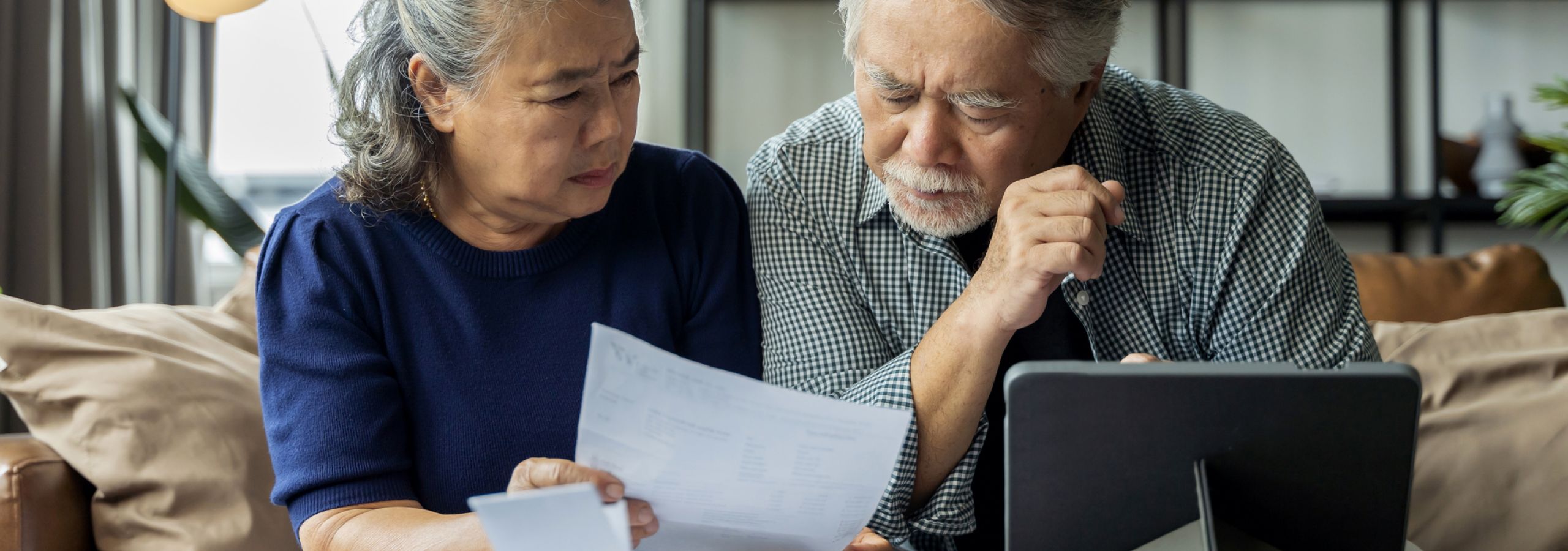 A white-haired Asian couple compare their bills to a computer tablet and realize their data has been stolen.