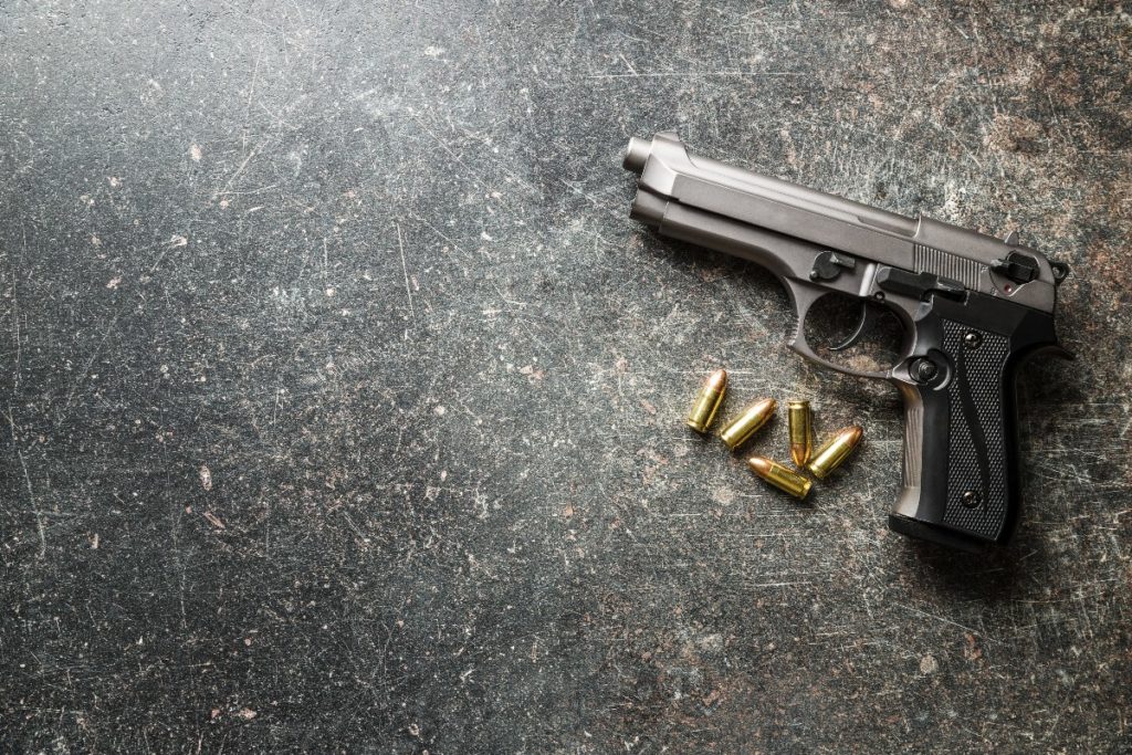 Silver and black 9mm handgun resting on ground with bullets