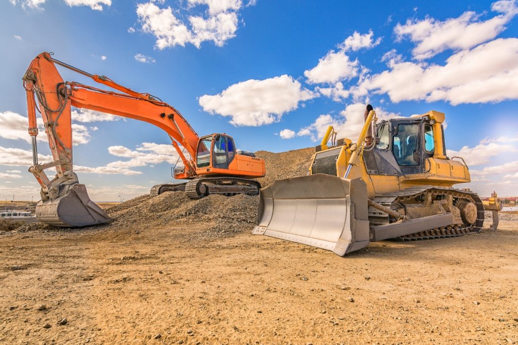 An orange excavator and yellow steer skid stand on a construction site.